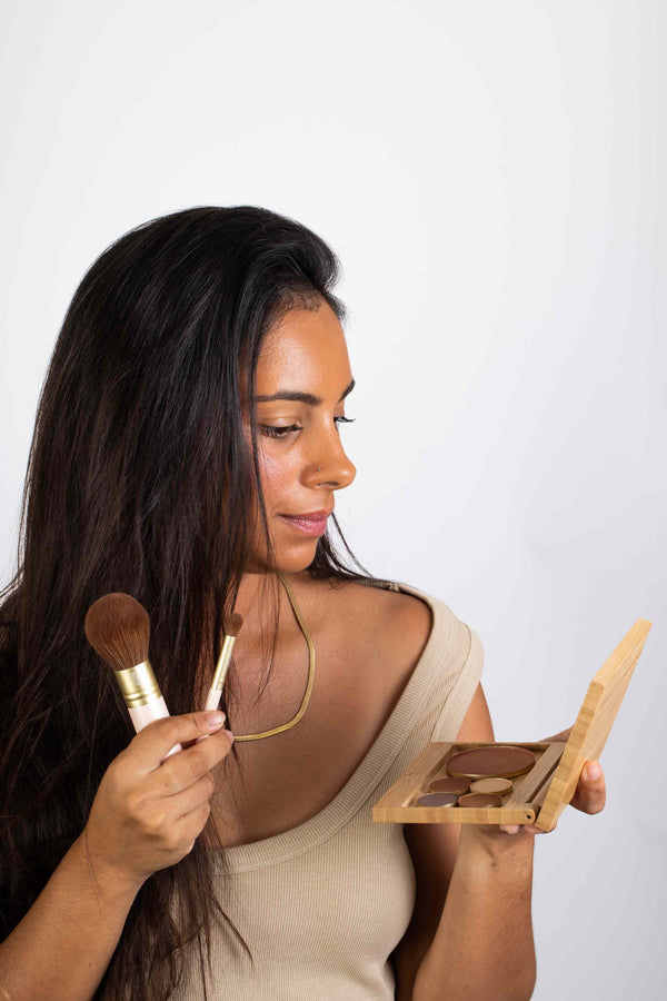 Scoop Whole Beauty model holding sustainable refillable bamboo multi compact, kabuki brush and eyeshadow brush. 