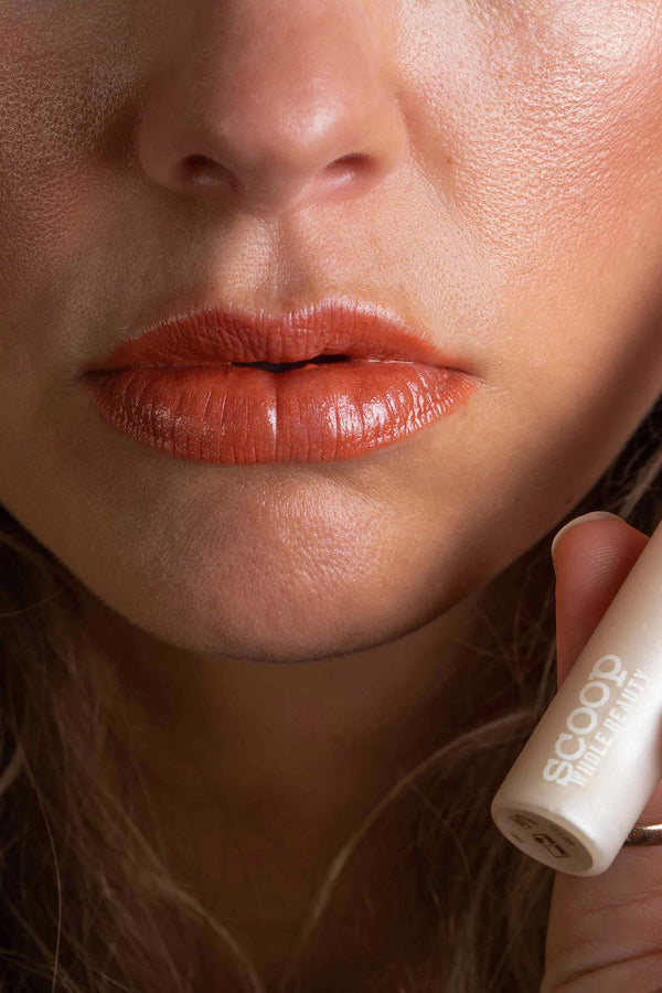 Scoop Whole Beauty model wears natural, non toxic lipgloss as topcoat over peach lipstick- clear