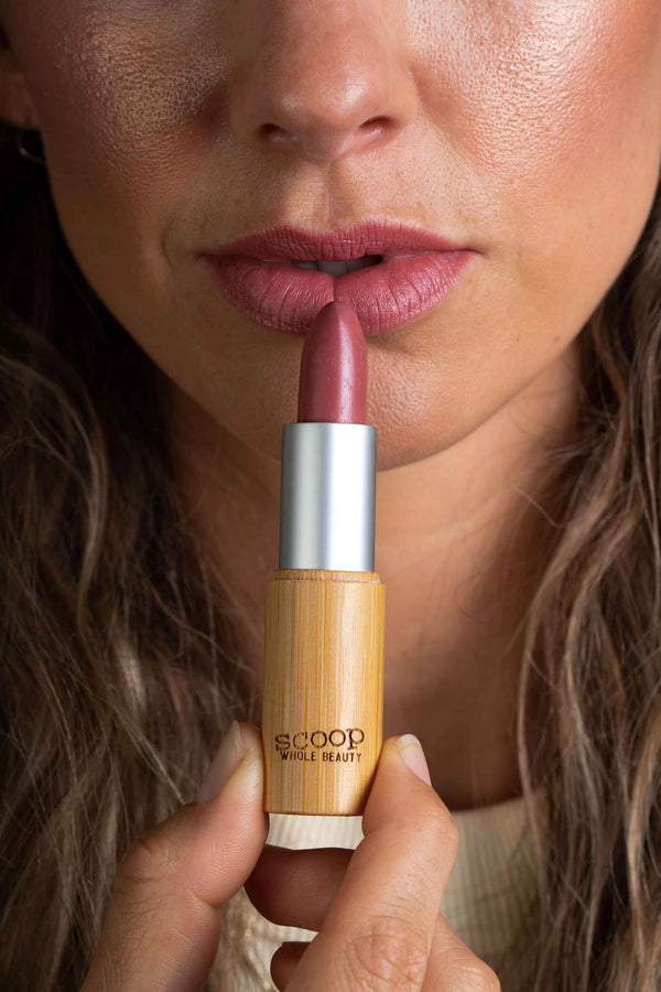 Scoop Whole Beauty model applies natural lipstick, shade rose, in sustainable bamboo tube. Ultra hydrating formula and long lasting effect