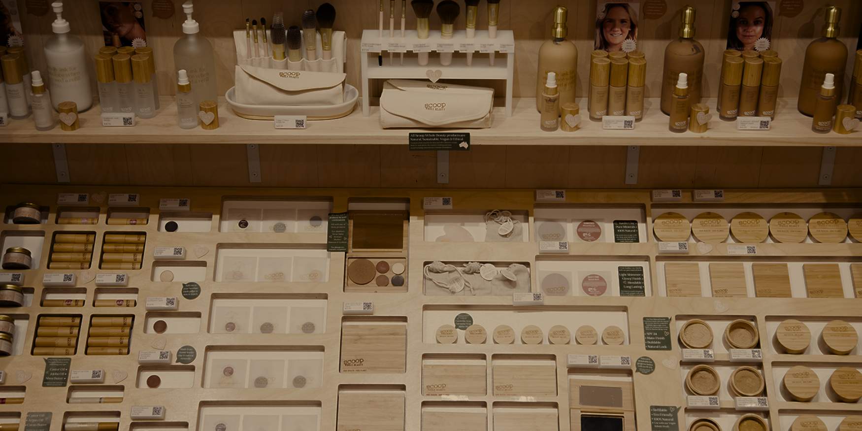 A refillable beauty bar by Scoop Whole Beauty featuring sustainable makeup, bamboo-packaged skincare, and eco-friendly cosmetics on a neatly organized wooden display.