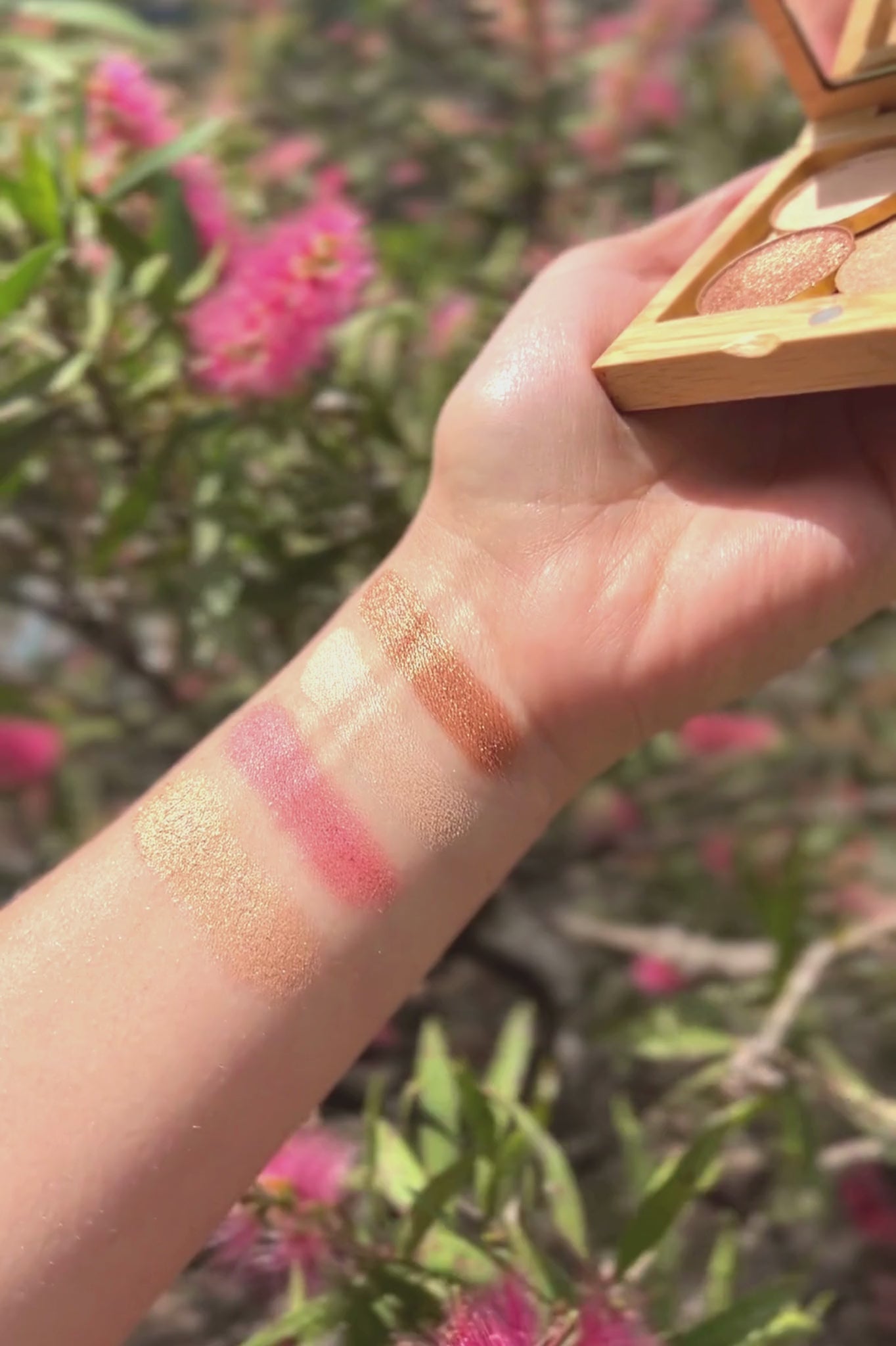 A six second clip of hand swatches of the Pink Lake Eyeshadow Palette. The hand is holding the palette in an outdoor setting.