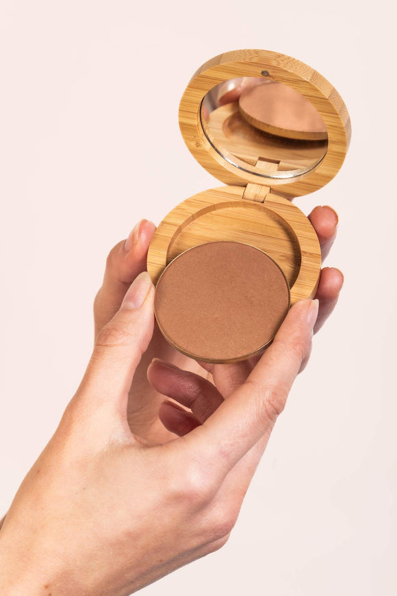Scoop Whole Beauty sun-kissed natural mineral bronzer refill being inserted into sustainable bamboo mirror compact