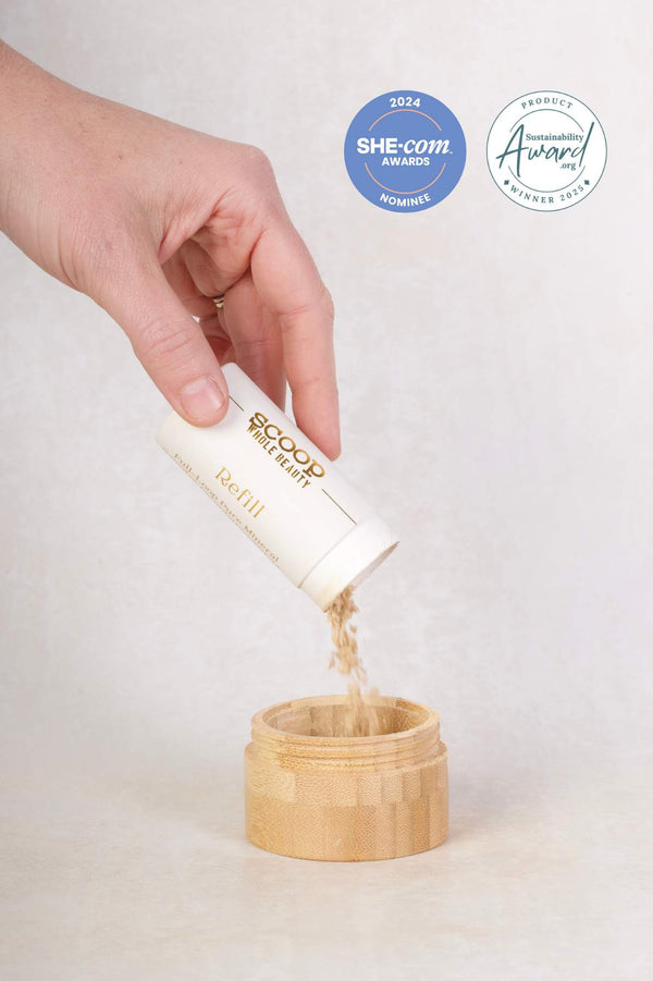 Scoop Whole Beauty full loop pure mineral powder foundation with SPF being poured from a cardboard tube with gold writing into a bamboo foundation box